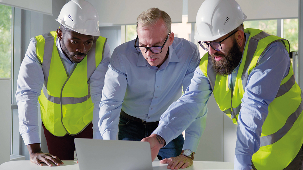 Architects discussing blueprint on laptop with construction manager in office